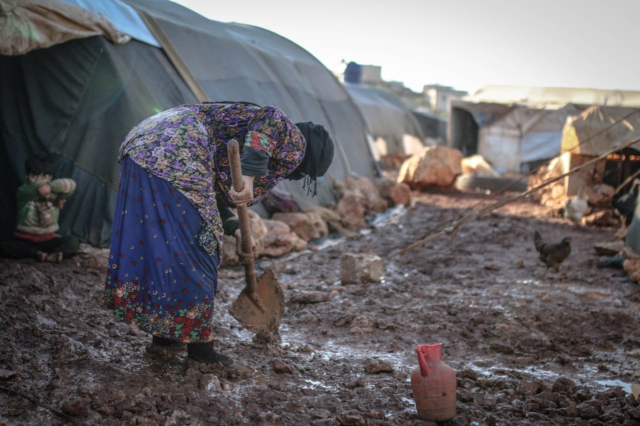 An elderly woman works in the mud at an outdoor refugee camp in Idlib, Syria.